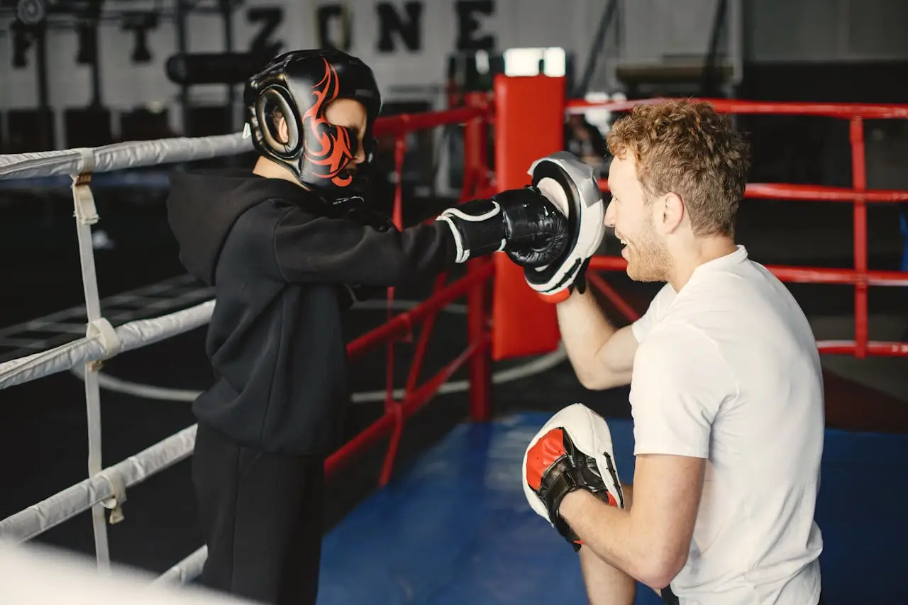 Boy in boxing gear practices punches with coach in gym training session.